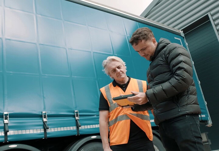 Logistics professional discussing delivery details with driver beside a truck, highlighting Microlise's journey management technology for efficient fleet operations.