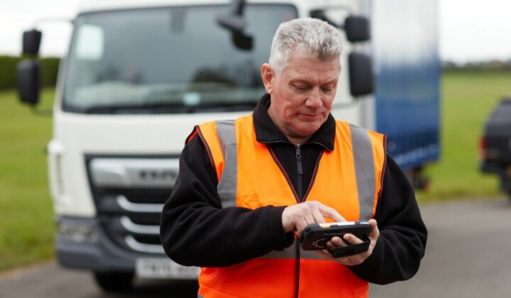 man using microlise tms on a mobile device standing in front of a lorry