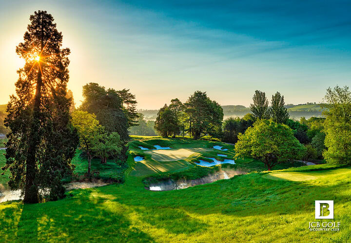 Lush green golf course with sand traps and water hazards under a bright sunrise, ideal for promoting luxury golf experiences and scenic leisure activities.