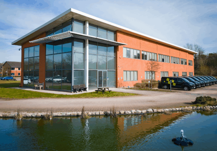 Modern office building with glass facade and parking at Microlise headquarters in the UK, surrounded by natural water features and greenery.