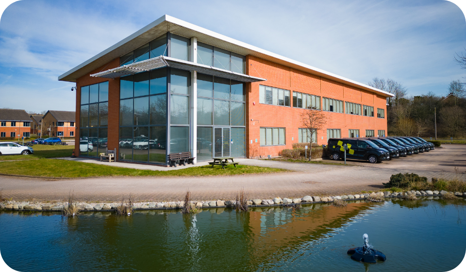 Modern corporate office building with glass facade and company branding, set in a scenic environment near a pond, representing innovative logistics and fleet management solutions.