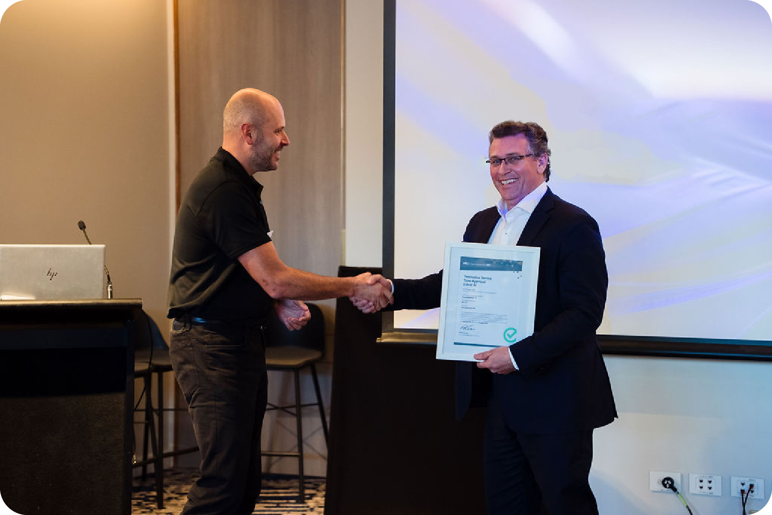 Award ceremony at Microlise logistics technology event in the UK with two men shaking hands, one presenting a framed certificate.