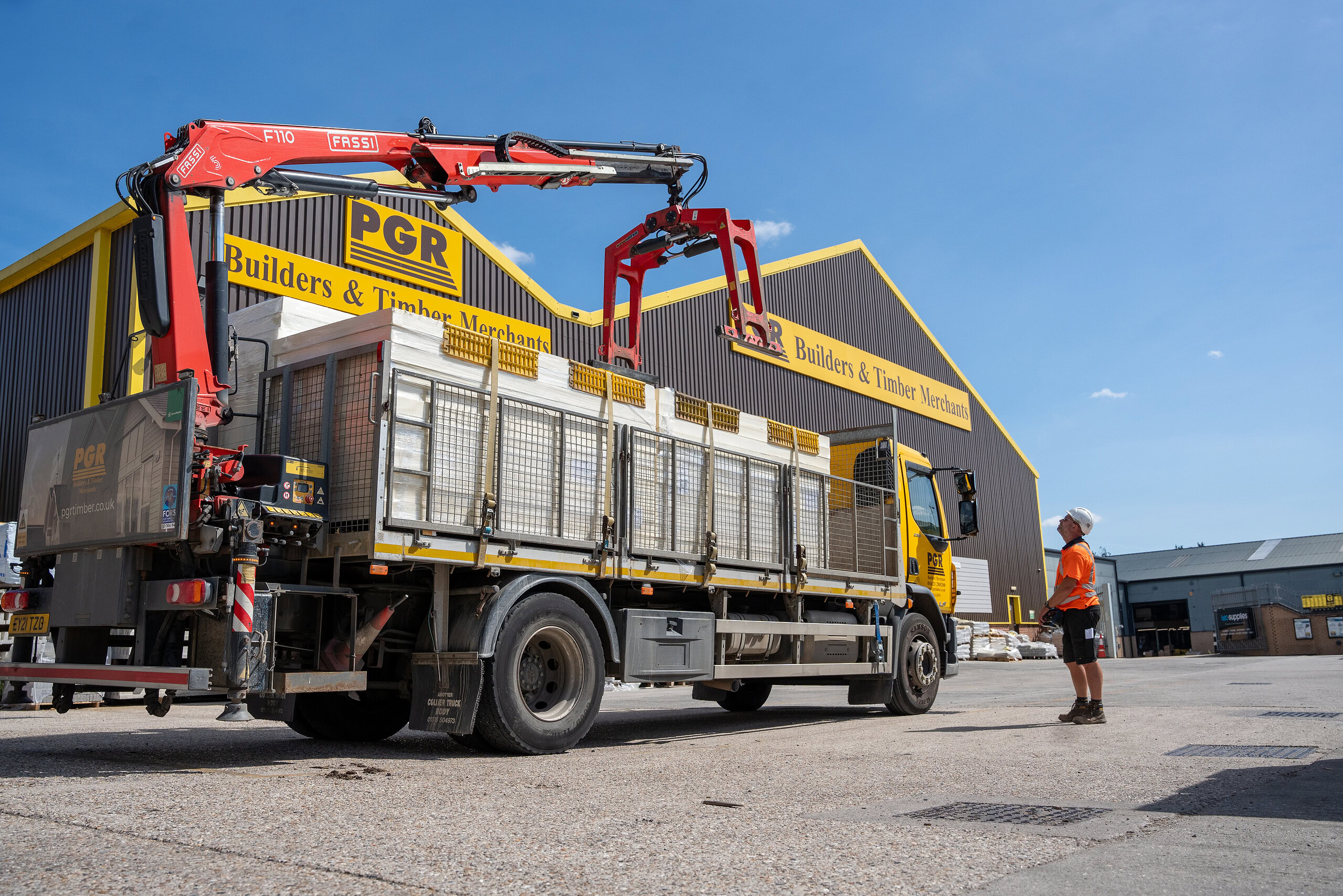 Forklift truck unloading at a timber merchant with a worker overseeing; highlights logistics, fleet management, and supply chain solutions by Microlise for the construction and timber industry.