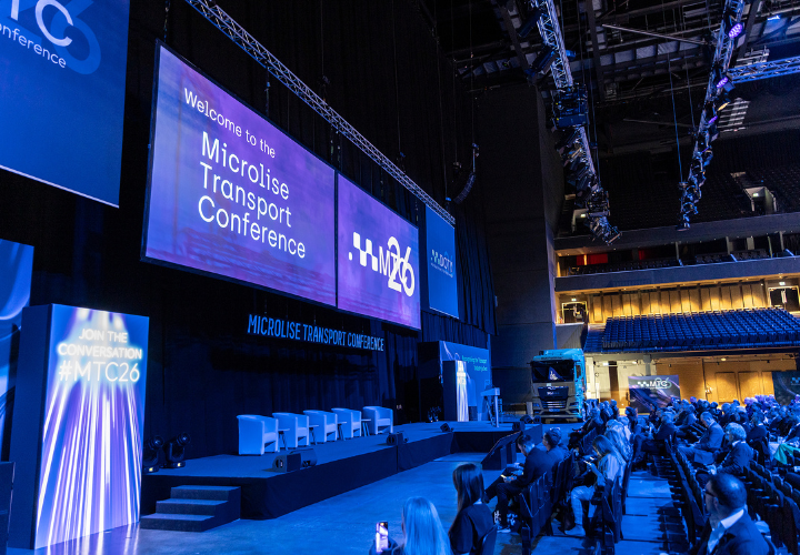 Advanced transport technology conference stage with large digital screens displaying Microlise branding and event information, attended by industry professionals.