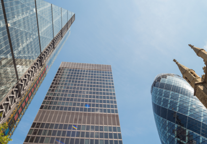 View of modern skyscrapers in London, including the Gherkin, under a clear blue sky.