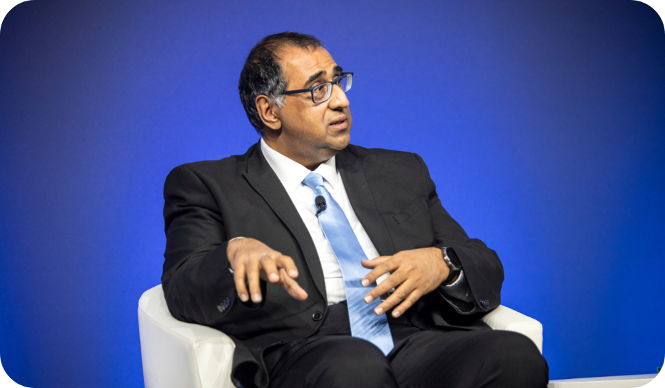 Professional man in a suit speaking during a panel discussion against a blue background.